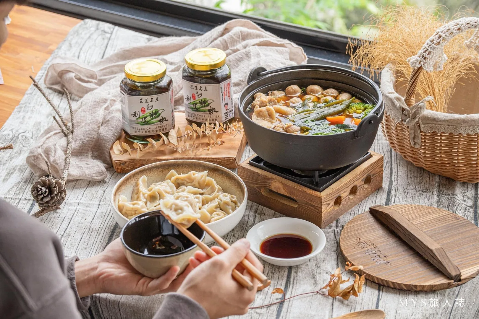 餐桌擺盤照：兩罐剝皮辣椒、鍋物與一碗水餃，手持碗筷正在取食，呈現剝皮辣椒的家常料理搭配