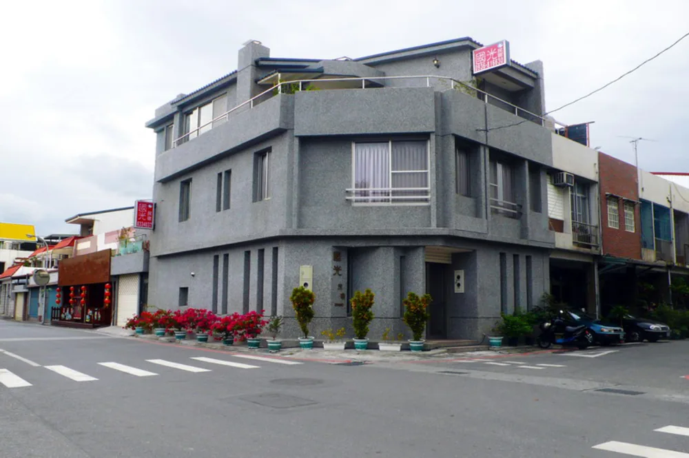 灰色三層角屋民宿外觀，門口及路邊擺放多盆花卉，屋頂招牌寫有「國光民宿」