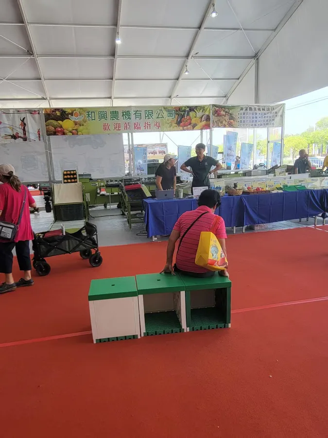 MECube無限方塊｜展場實拍：民眾於紅地毯上試坐模組化單人座椅，背景為展覽攤位