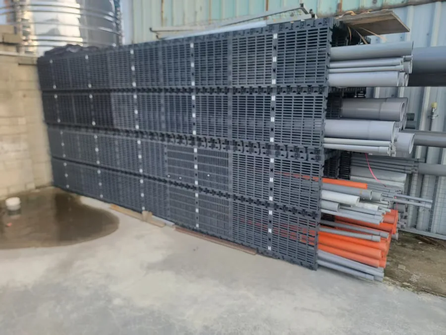 MECube無限方塊 現場實拍：大量深灰色模組化格柵垂直堆放於廠區倉儲旁，旁邊並置管材
