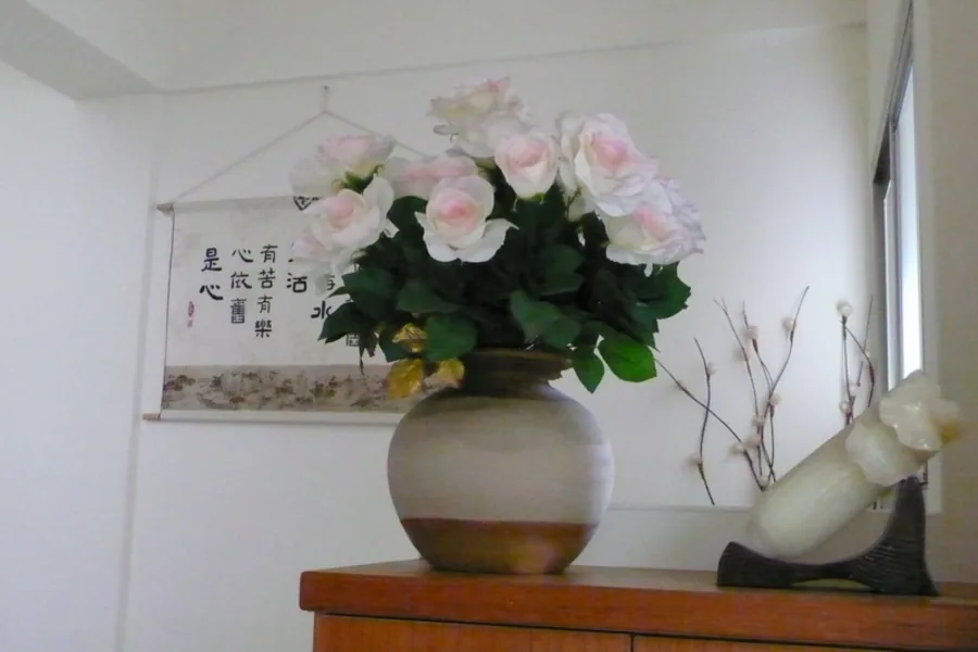 粉色玫瑰花束插於陶瓷花瓶，置於木櫃前並有掛軸書法作為背景