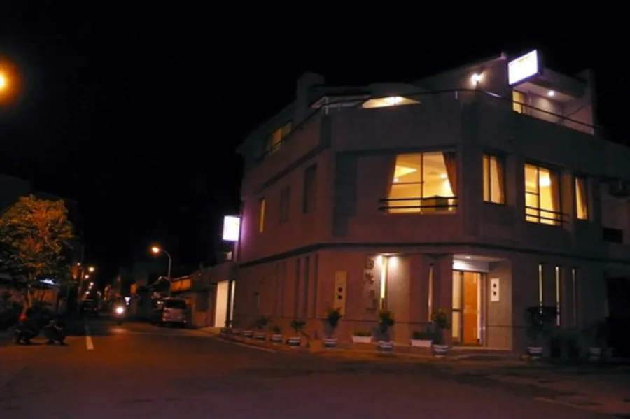 夜間街道角落的民宿外觀，三層樓建築窗內燈光與門廳出入口