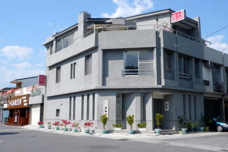 白天外觀：灰色三層樓民宿立面與門前排列的花盆